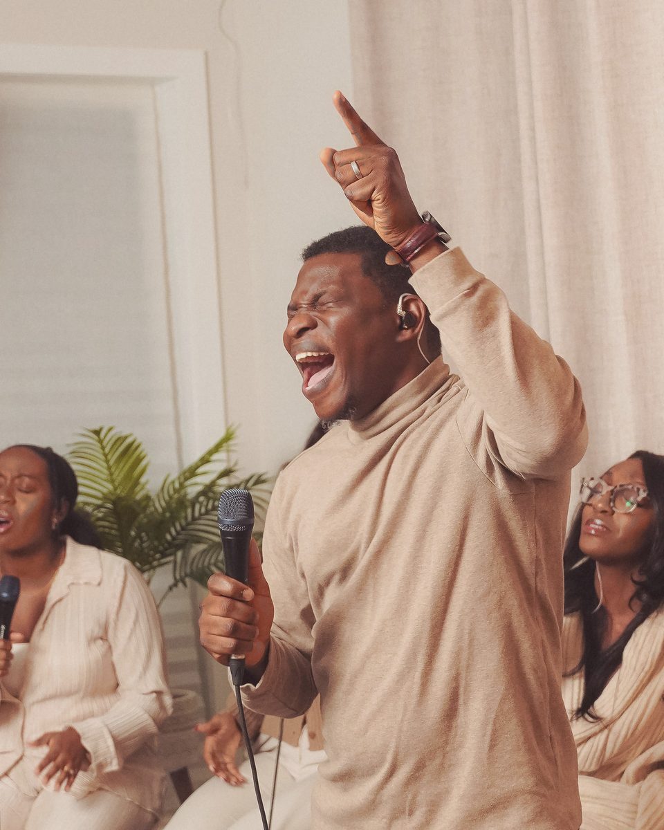 Victor leading worship with one hand raised, singers seated behind him, at Before The Throne in a living room in Ottawa