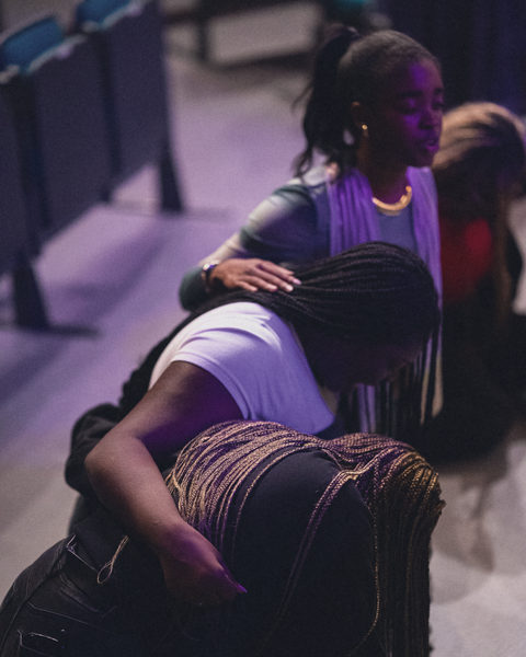 Three worshippers bow low in prayer, one resting her hand on another’s back