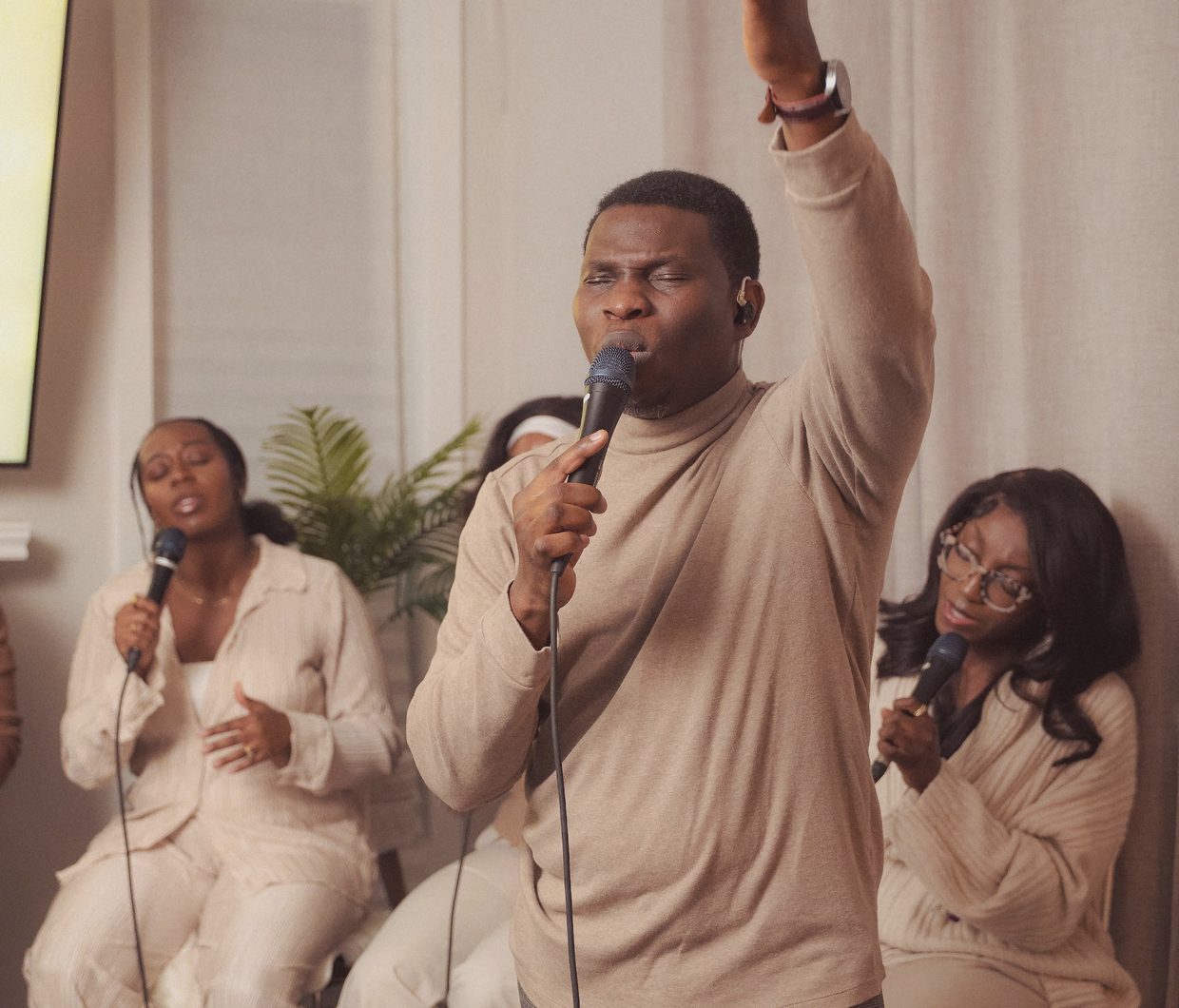Victor leading worship with his arm raised high, the worship team singing around him in a living room